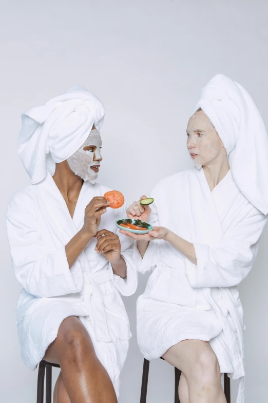 a couple of women sitting next to each other, an album cover, by Matija Jama, pexels contest winner, renaissance, skincare, offering a plate of food, white mask, white robes