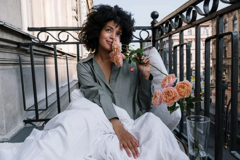 a woman sitting on a balcony with a bouquet of flowers, pexels contest winner, happening, flowing silk sheets, imaan hammam, curly haired, wearing a linen shirt