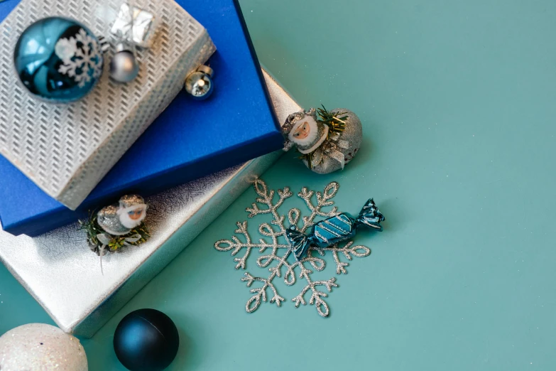 a pile of presents sitting on top of a blue table, a still life, inspired by Ernest William Christmas, trending on pexels, silver filigree details, teal paper, thumbnail, a high angle shot