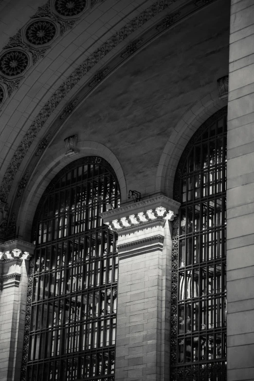 a black and white photo of a train station, neoclassicism, soft glowing windows, gotham, behind bars, arches