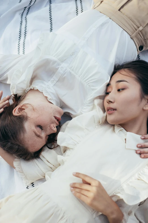 a couple of women laying on top of a bed, inspired by Ren Hang, trending on pexels, gutai group, wearing a white button up shirt, jingna zhang, facing each other, concert