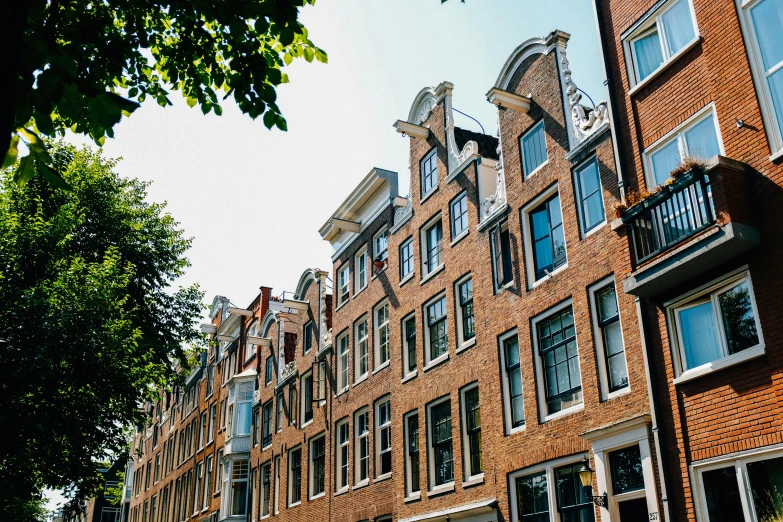 a row of brick buildings on a city street, by Jan Tengnagel, pexels contest winner, neoclassicism, dutch masters, summer afternoon, view from the ground, lush surroundings