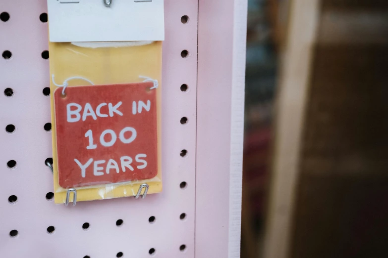 a sign that says back in 100 years hanging on a wall, by Rachel Reckitt, trending on unsplash, folk art, stood in a supermarket, cardstock, old retro museum exhibition, pink