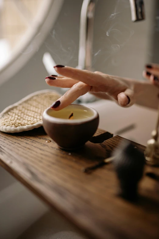 a wooden table topped with a bowl of food next to a faucet, by Julia Pishtar, trending on pexels, renaissance, forming a burning hand spell, organic seductive geisha, candle wax, morning haze