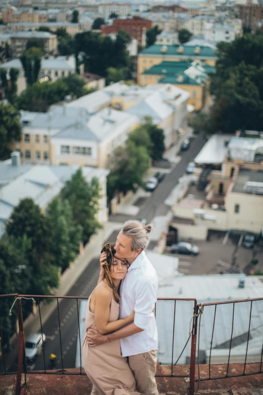 a man and a woman standing on top of a building, a picture, by Serhii Vasylkivsky, lush surroundings, hug, looking down on the camera, 000 — википедия