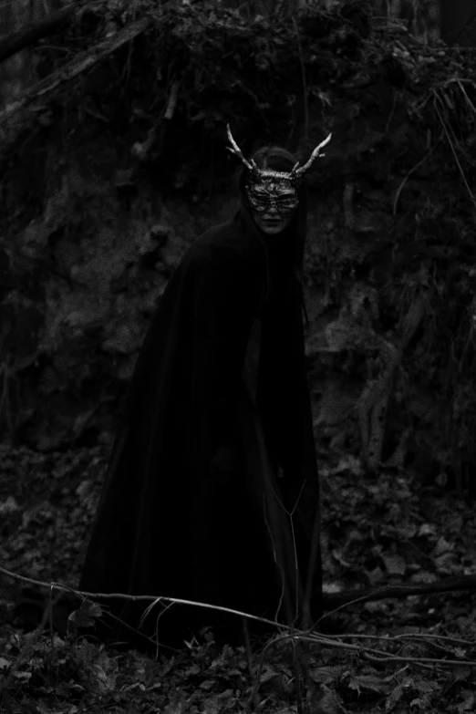 a black and white photo of a man with horns, an album cover, inspired by Nicola Samori, tumblr, wearing in black cloak, masked, anthropomorphic female deer, ✨🕌🌙