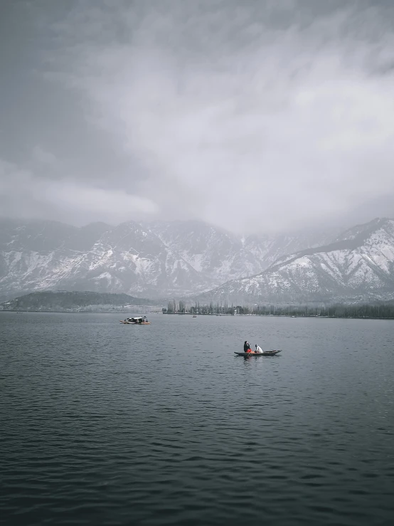 a couple of people in a boat on a lake, grey sky, snowy peaks, unsplash 4k, high quality product image”