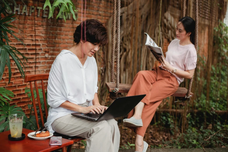 a woman sitting on a swing using a laptop computer, inspired by Ruth Jên, pexels contest winner, happening, two women, sitting on a mocha-colored table, sitting in the garden, patiphan sottiwilaiphong