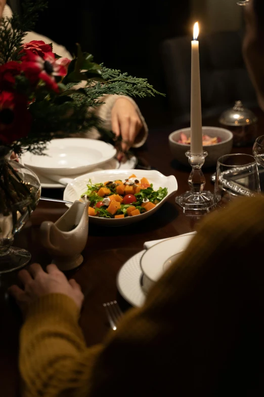 a group of people sitting around a dinner table, vegetables on table and candle, subtle details, ignant, salad