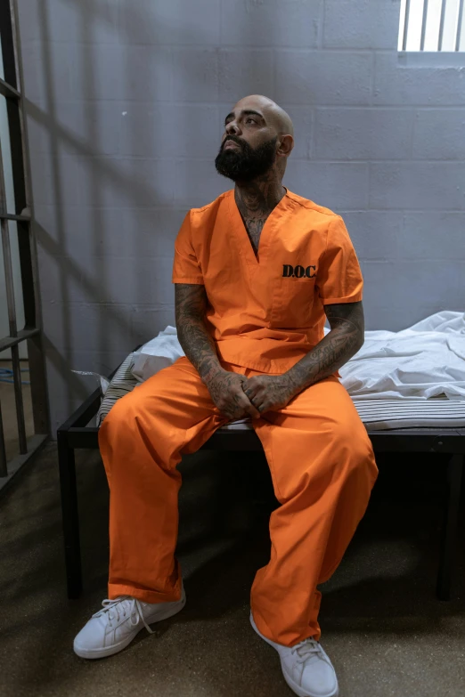 a man sitting on a bed in a jail cell, trending on reddit, wearing orange prison jumpsuit, mc ride, gettyimages, ( ( theatrical ) )