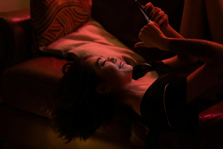 a woman laying on a couch holding a cell phone, inspired by Nan Goldin, trending on pexels, happening, 8 0 s asian neon movie still, happy lighting, chiaroscuro lighting, drunk
