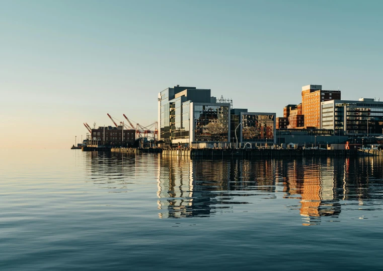 a large body of water with buildings in the background, by Carey Morris, pexels contest winner, modernism, shipyard, cinematic morning light, foster and partners, ballard