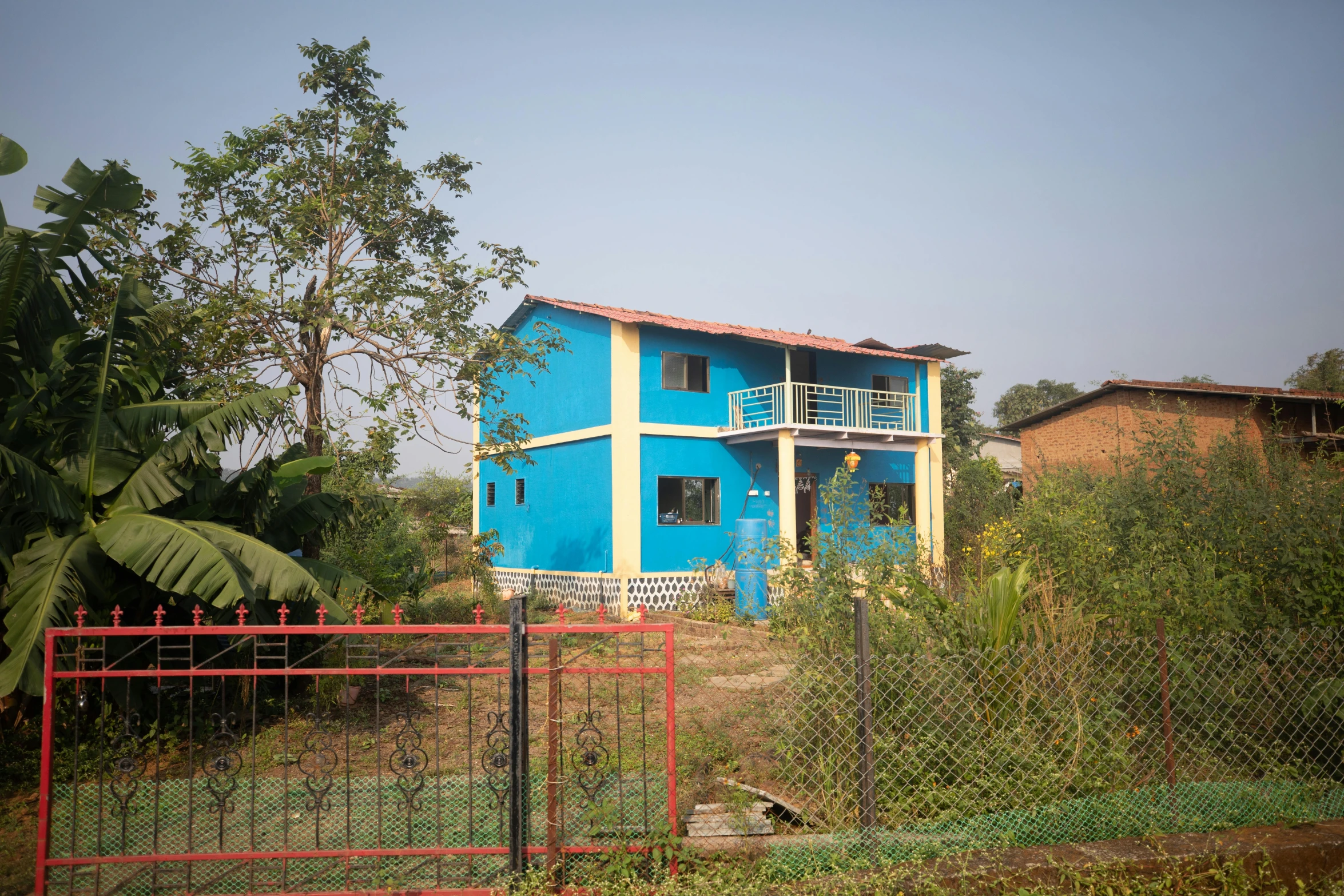 a blue house behind a chain link fence, bengal school of art, in the countryside, passive house, profile image