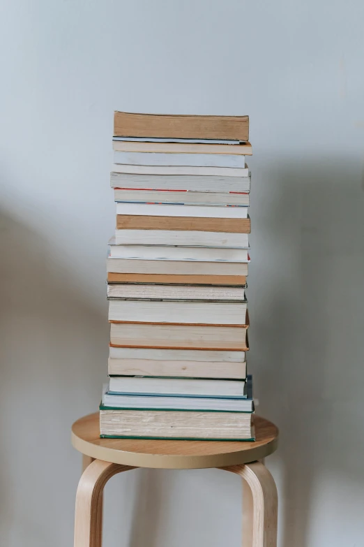 a stack of books sitting on top of a wooden stool, on a white table, - 9, tall thin build, abcdefghijklmnopqrstuvwxyz