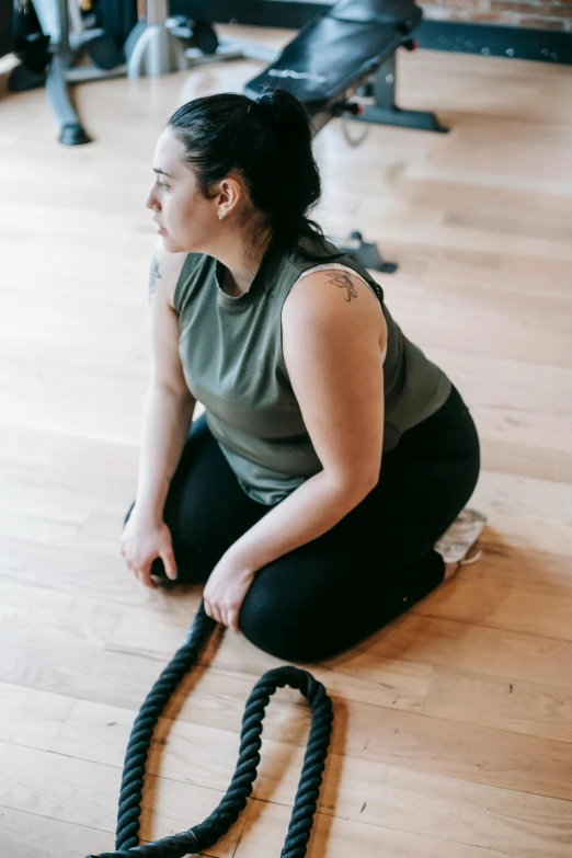 a woman sitting on the floor with a rope, she is wearing a black tank top, kaitlyn michelle siragusa, profile image, sweat and labour