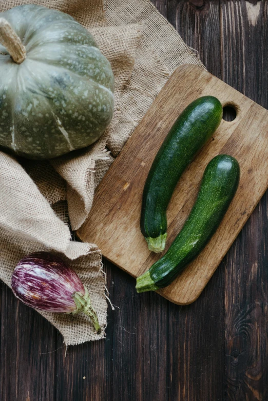 a couple of zucchini sitting on top of a wooden cutting board, unsplash, renaissance, green and purple, square, ingredients on the table, no - text no - logo