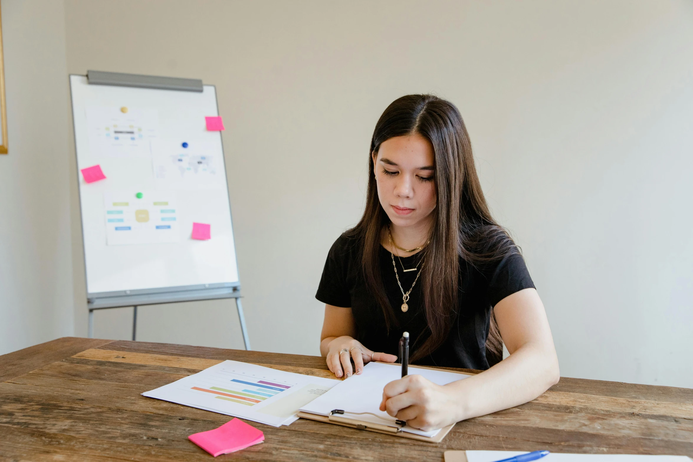 a woman sitting at a table writing on a piece of paper, a drawing, by Olivia Peguero, pexels contest winner, whiteboards, avatar image, marketing photo, 9 9 designs