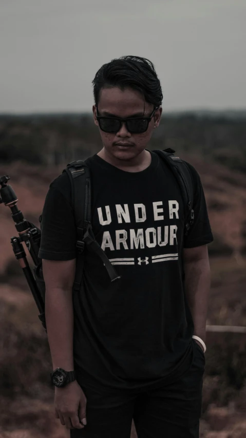 a man standing in a field with a gun, inspired by Rudy Siswanto, unsplash, sumatraism, wearing a black!! t - shirt, minimal design armor style, underground, sport t-shirt