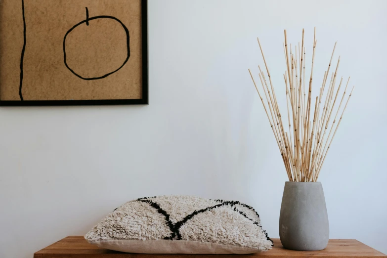 a vase sitting on top of a wooden table next to a pillow, inspired by Esaias Boursse, minimalism, macrame, detailed product image, small details, rectangular