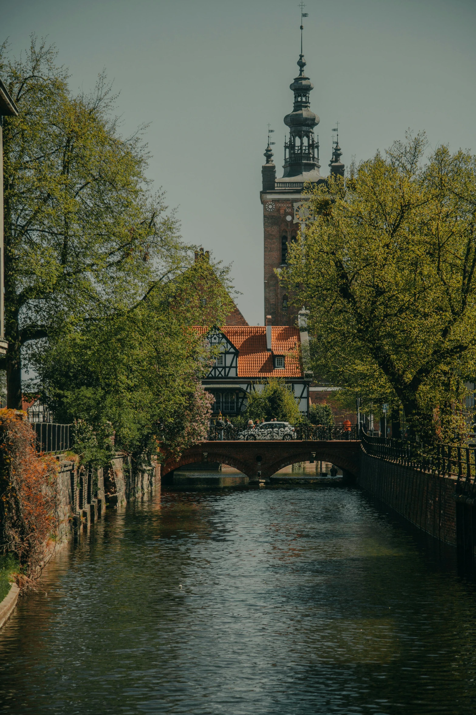 a river next to a building with a clock tower in the background, a photo, by Jan Tengnagel, banner, square, swanland, red castle in background