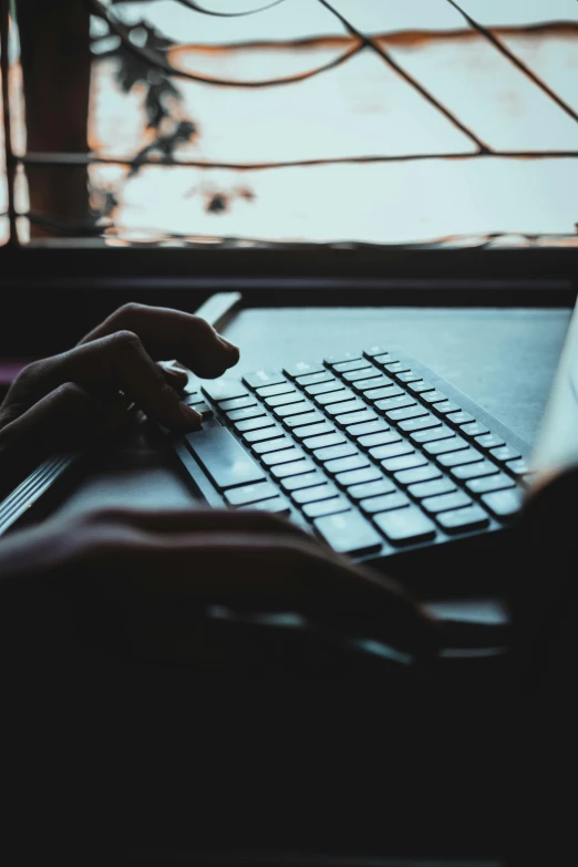 a person typing on a laptop in front of a window, by Carey Morris, pexels, paul barson, digital image, evening time, bottom angle