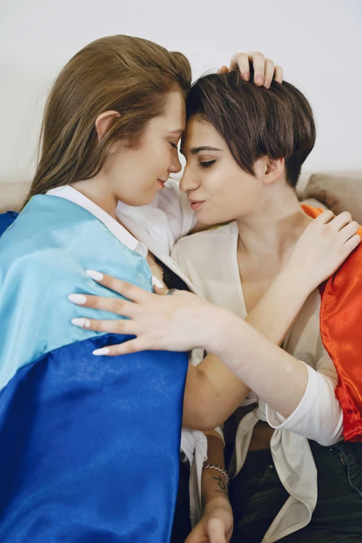 a couple of women sitting on top of a couch, trending on reddit, romanticism, wearing a barca cape, lesbian embrace, close up half body shot, vexillology