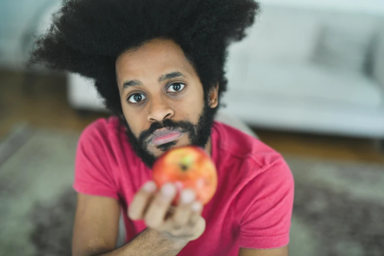 a close up of a person holding an apple, pexels contest winner, magic realism, black curly beard, macron with afro hair, light stubble with red shirt, sentient fruit