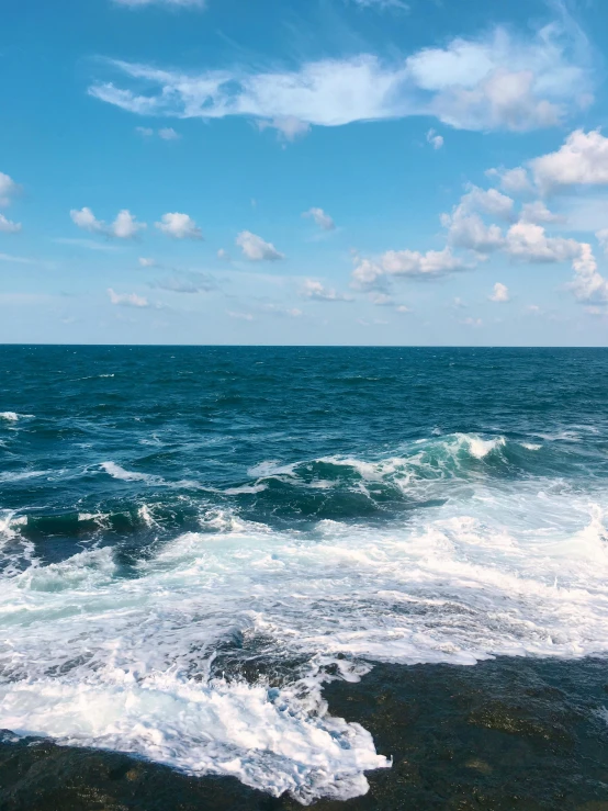 a large body of water sitting on top of a rocky beach, rough waves, blue skies, profile image, next to the sea