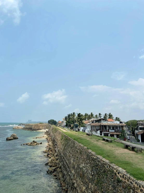 a stone wall next to a body of water, tropical coastal city, sri lankan landscape, walking to the right, preserved historical