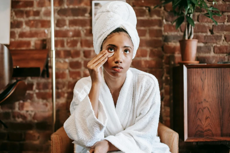 a woman sitting in a chair with a towel on her head, pexels contest winner, bags under eyes, manuka, wearing a white robe, dark-skinned