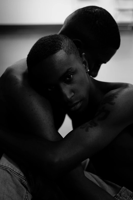 a couple of men sitting next to each other, a black and white photo, by Terrell James, hugging his knees, pitch black skin, playboi carti, looks sad and solemn