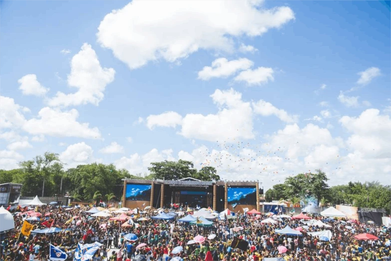 a large crowd of people with umbrellas in front of a stage, epic blue sky, argentina flags behind, full trees, 2019 trending photo