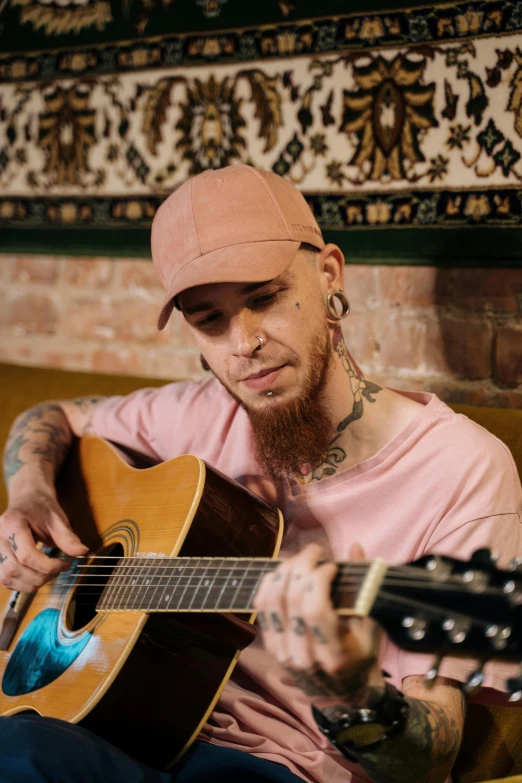 a man sitting on a couch playing a guitar, inspired by Seb McKinnon, tattooed face, he is wearing a hat, soft shade, dale odell