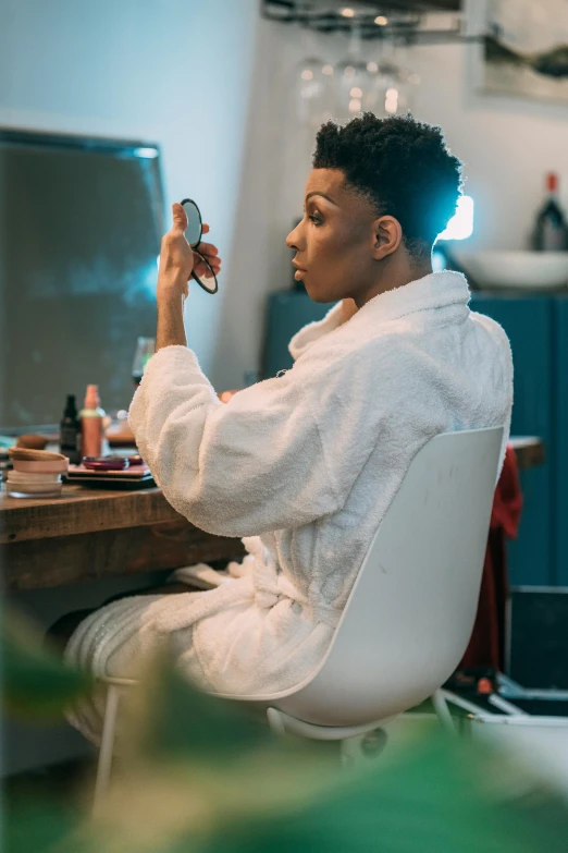 a woman in a bathrobe sitting at a desk, trending on pexels, afrofuturism, putting makeup on, androgynous male, wearing white cloths, profile image