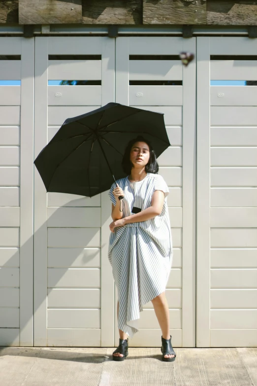 a woman standing in front of a garage holding an umbrella, by Basuki Abdullah, unsplash, wearing nanotech honeycomb robe, wearing toga, casual black clothing, dwell