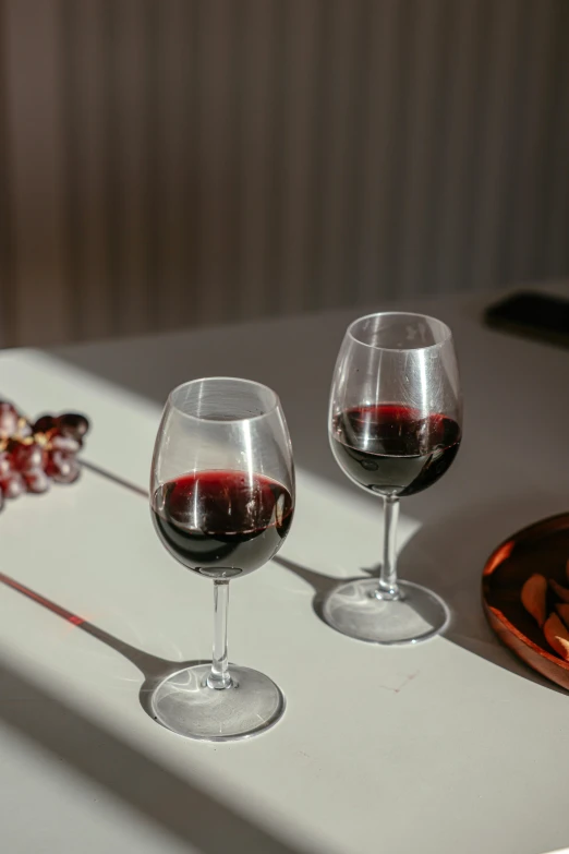 a couple of wine glasses sitting on top of a table, pexels contest winner, red wine, amber glasses, sydney hanson, grape