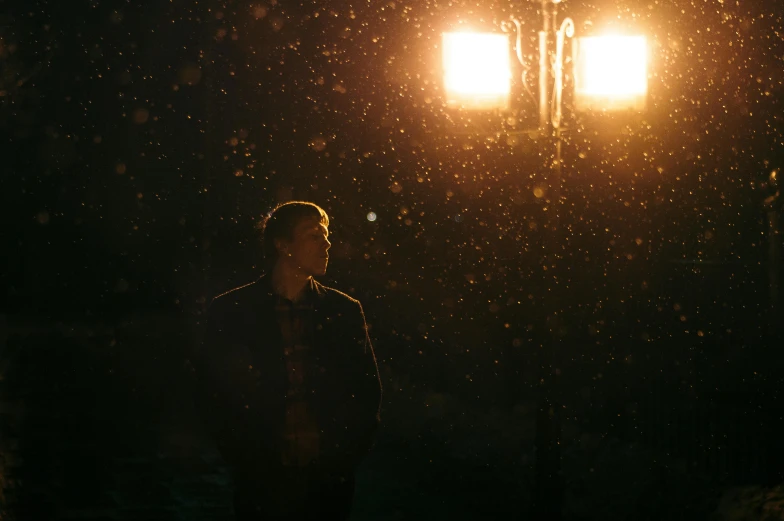 a man standing under a street light at night, an album cover, pexels contest winner, conceptual art, snowing, backlit portrait, golden light, standing in a dimly lit room