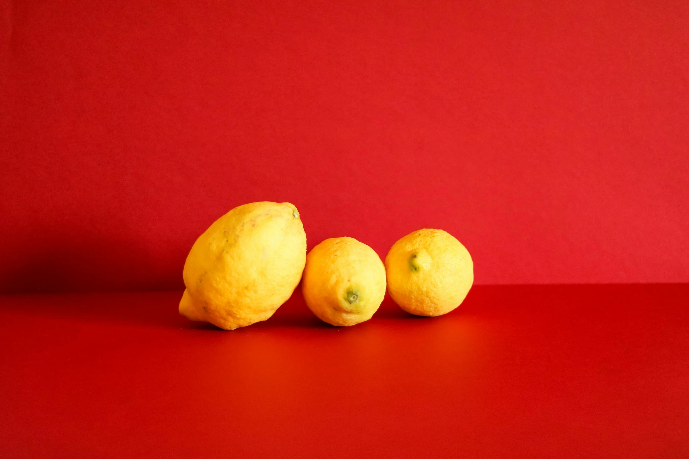 three lemons sitting next to each other on a red surface, by Carey Morris, pexels contest winner, pale yellow walls, demna gvasalia, medium format, coloured