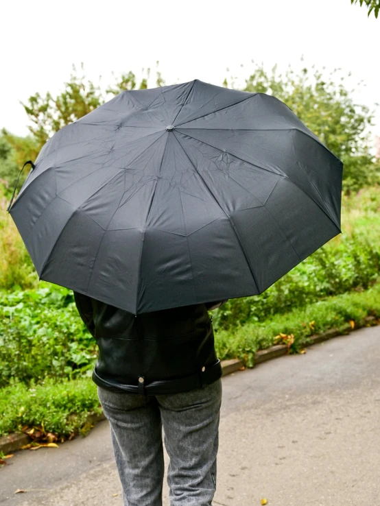 a person walking down a road holding an umbrella, official product photo, 3 / 4 view from back, main colour - black, vista view