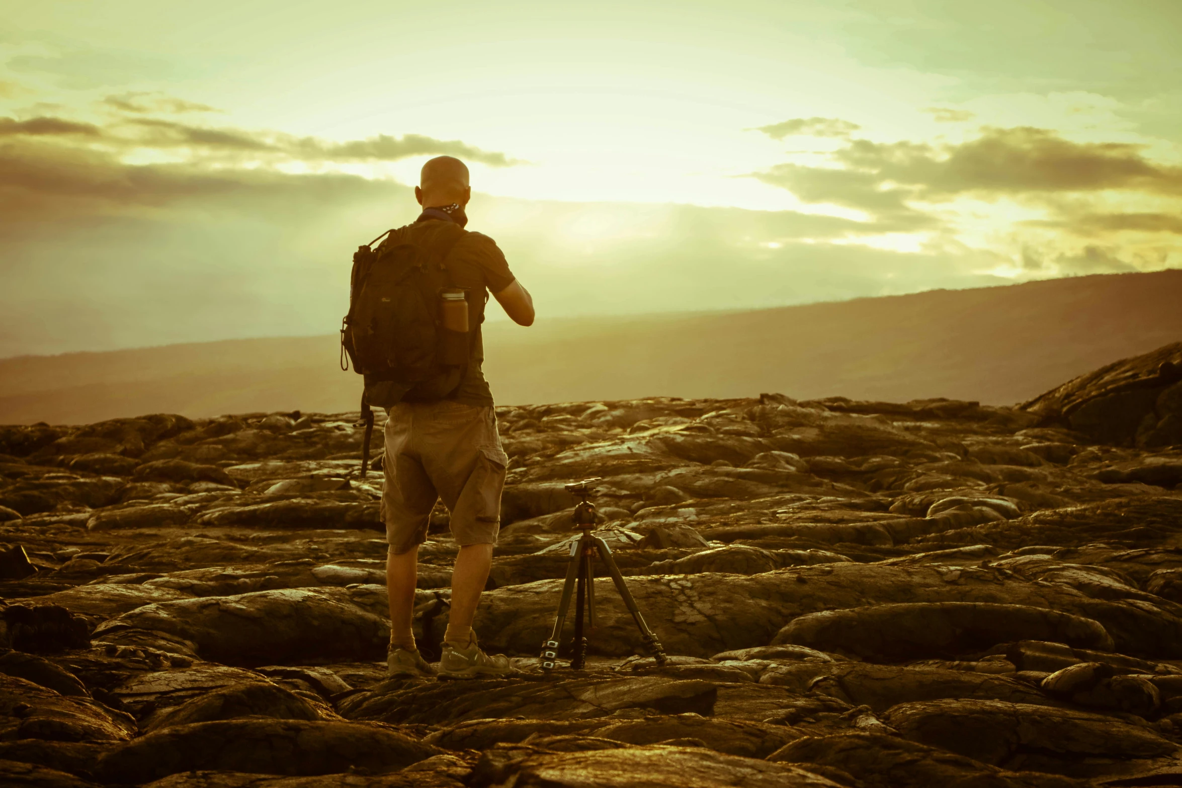 a man standing on top of a rocky hill, a picture, by Lee Loughridge, pexels contest winner, visual art, holding a big camera, goldenhour, big island, walking away from camera