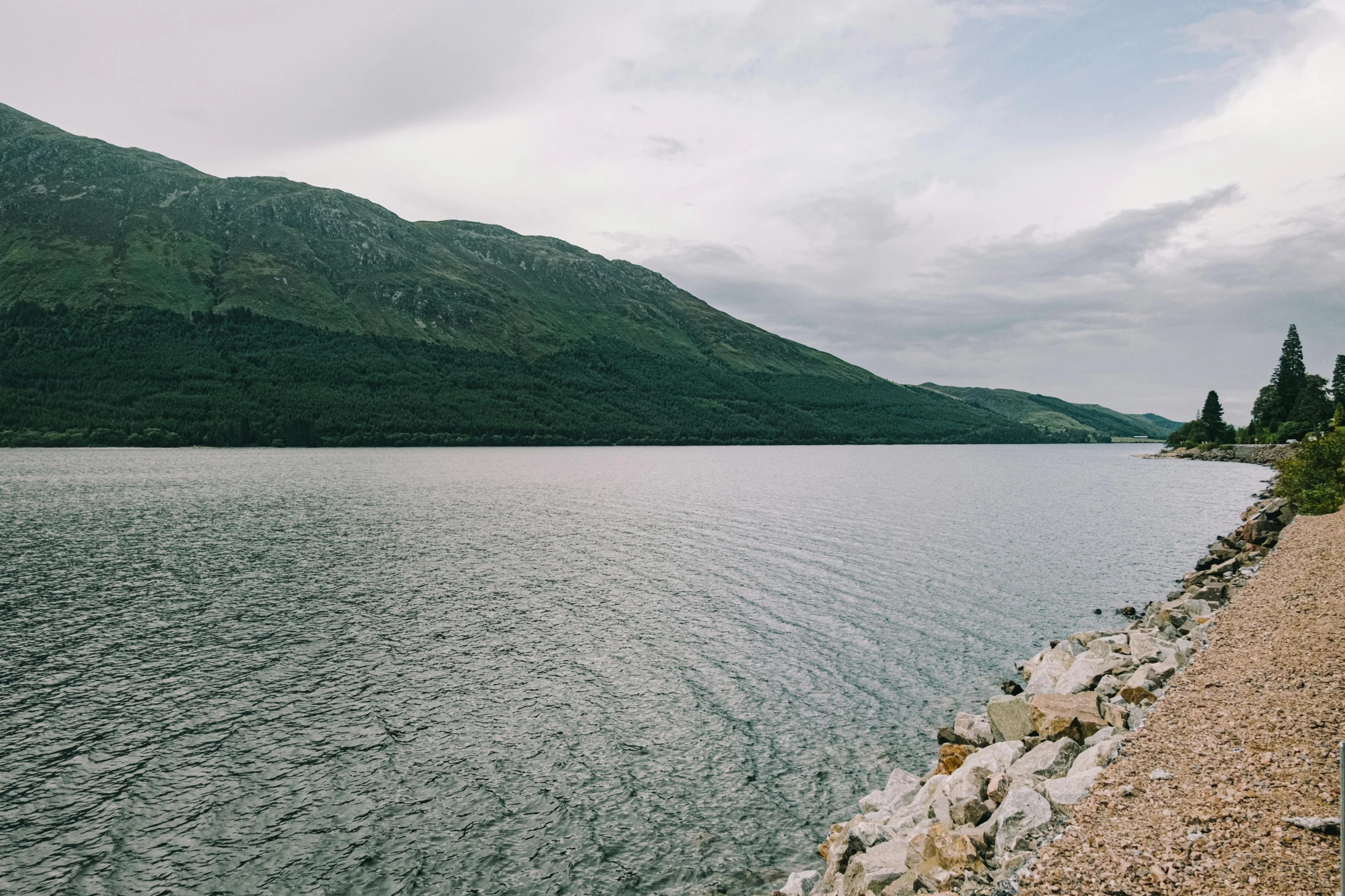 a motorcycle parked on the side of a road next to a body of water, by Carey Morris, unsplash, loch ness monster, panorama, where a large