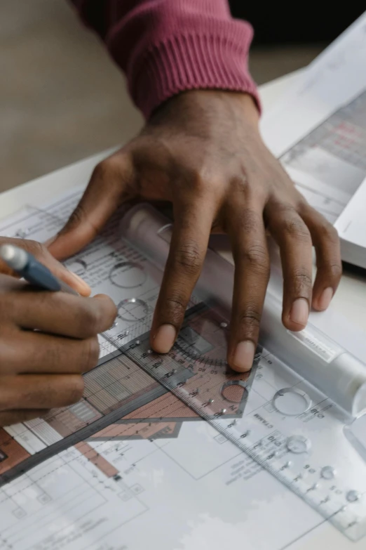 a person sitting at a table with a pen and paper, visual art, building plans, big hands, brown, thumbnail