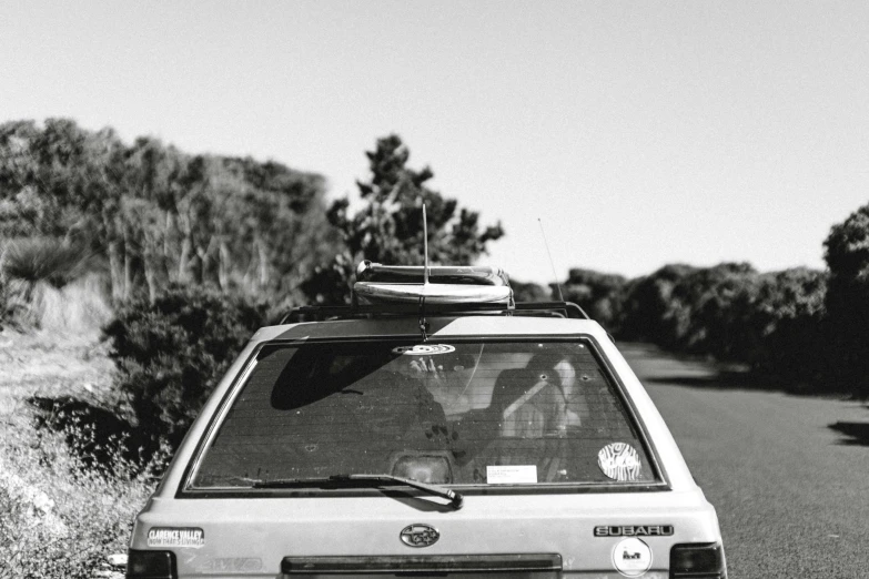 a black and white photo of a car with a surfboard on top, by Caro Niederer, lachlan bailey, ae 8 6, pilgrimage, jenny seville