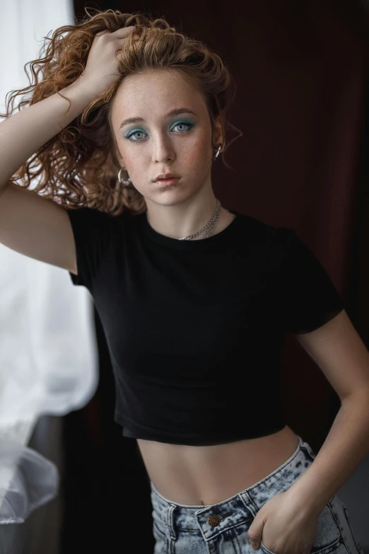 a beautiful young woman standing next to a window, a colorized photo, inspired by Elizabeth Polunin, trending on pexels, wearing a cropped black tank top, curly red hair, with blue eyes, on a white table