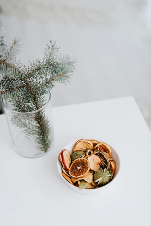 a white table topped with a bowl of dried fruit, by Jessie Algie, unsplash, evergreen branches, minn, indoor, crisps