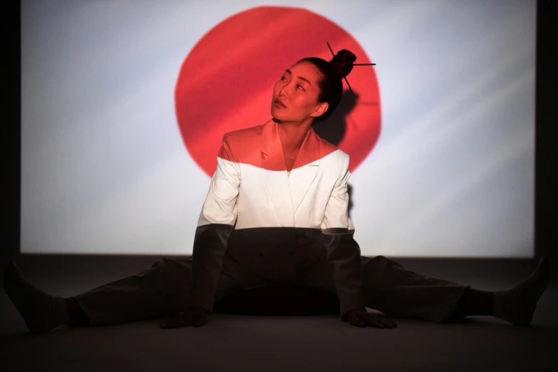 a woman sitting on the ground in front of a screen, inspired by Koson Ohara, unsplash, video art, grace jones, in a dojo, sun behind him, concert