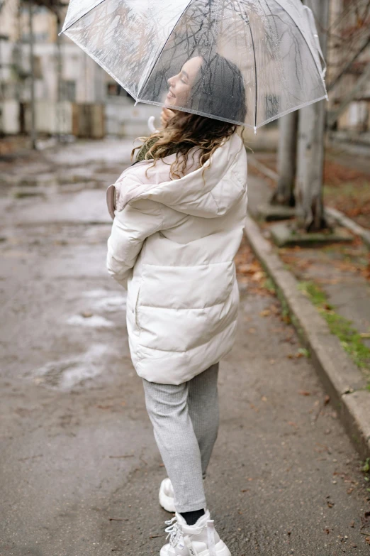 a woman walking down a street holding an umbrella, by Lucia Peka, unsplash, visual art, model wears a puffer jacket, silver，ivory, little kid, long shot from back
