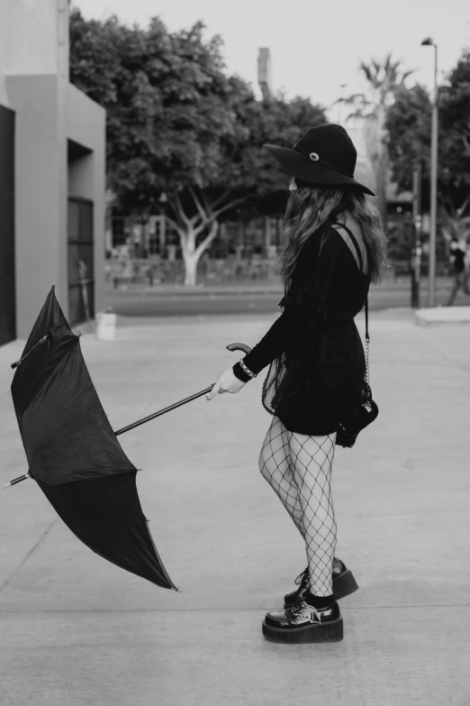 a black and white photo of a woman holding an umbrella, fishnet tights, tumblr aesthetic, black canary, a woman walking