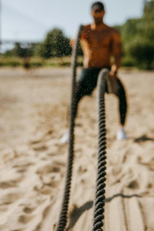 a man sitting on top of a rope on a beach, zoomed in, local gym, ((chains)), working out in the field