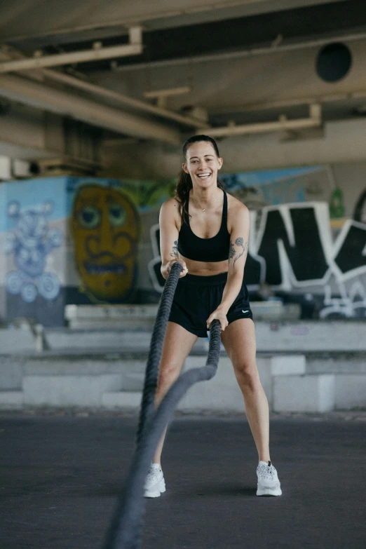 a woman holding a rope in a parking lot, she is wearing a black tank top, in a gym, kacper niepokolczycki, promo image